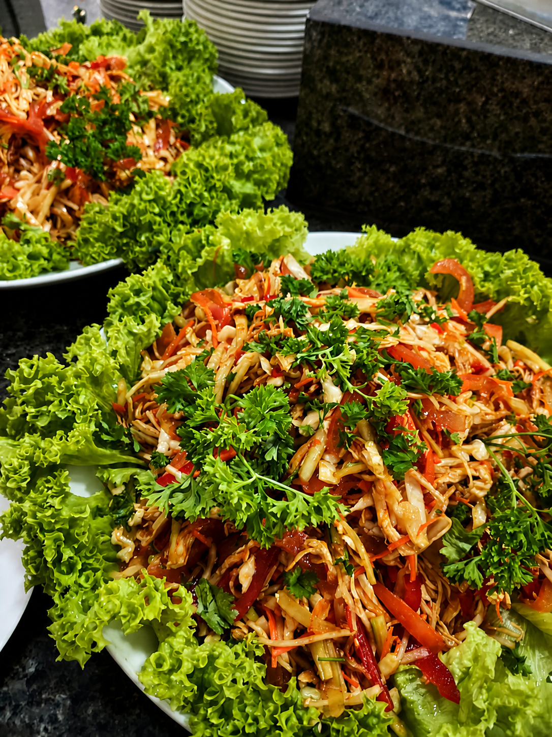 A shredded salad dressed with chilli and herbs, heaped on a bed of curly lettuce on a white platter.