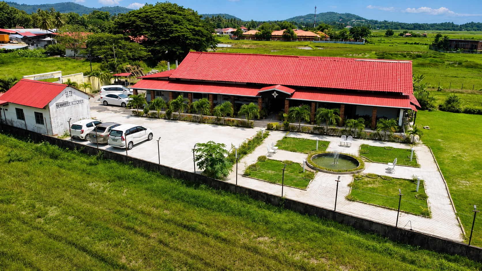 The restaurant from above: one long red-tiled roof, a front garden with a round pond and paved paths, and rice fields and hills all around it.