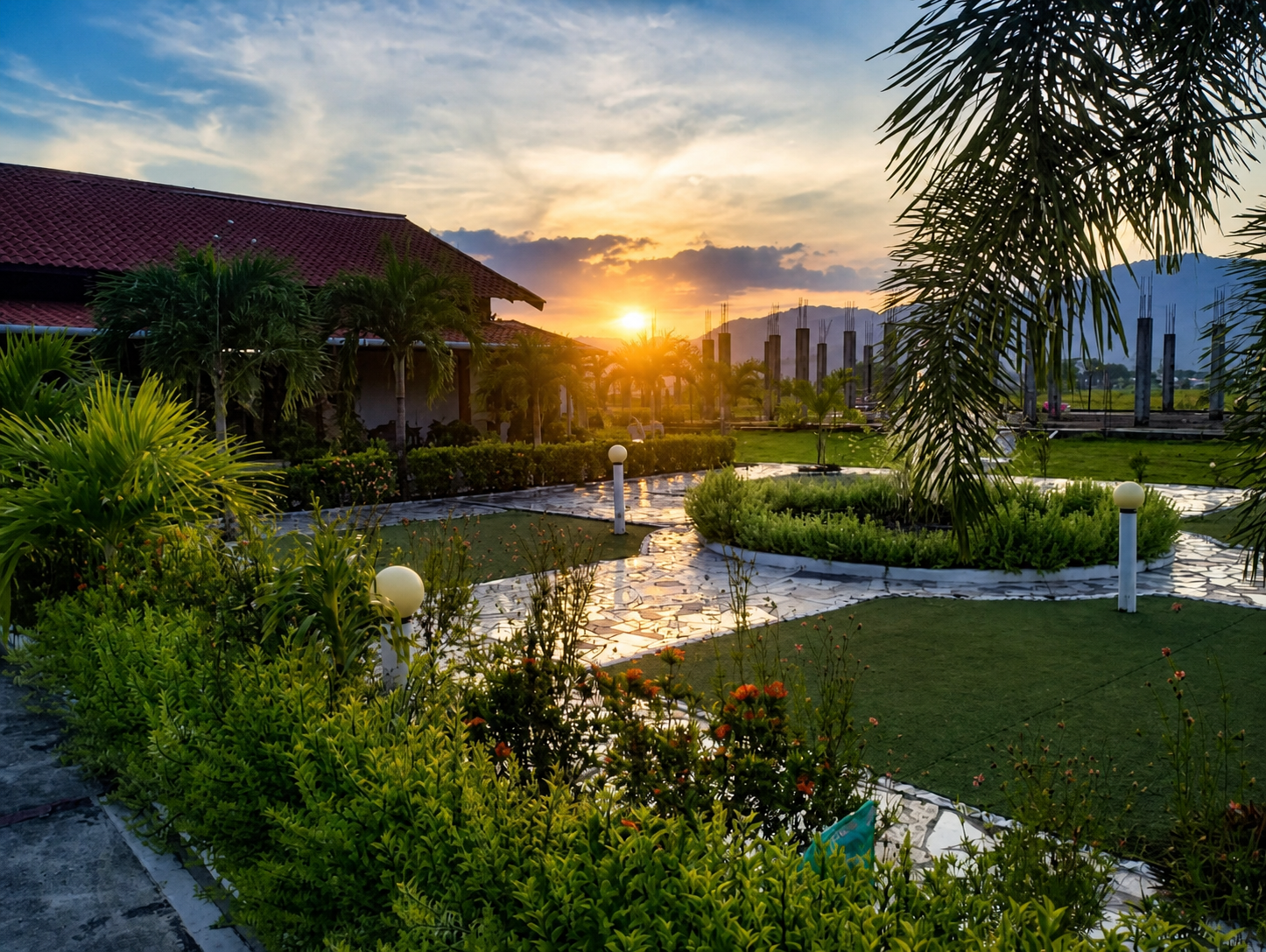 Sunset over the restaurant’s garden: paved paths, flowering beds and lawn in front of the building, with hills on the horizon.