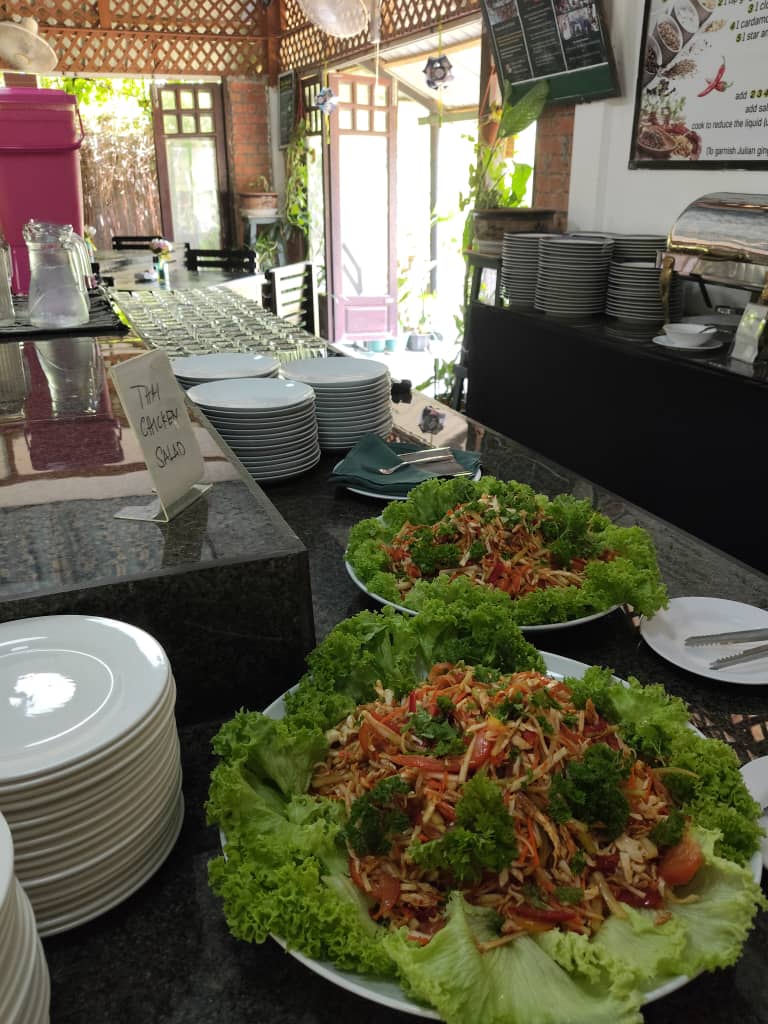 Two wide platters of shredded salad on curly lettuce beside stacks of plates, with the open doorway and the garden behind them.