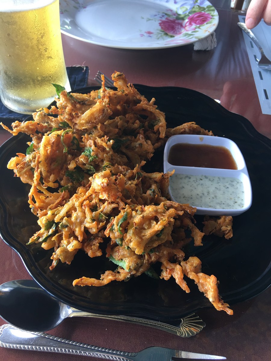 A heap of crisp vegetable fritters on a black plate with two small dipping sauces beside them.